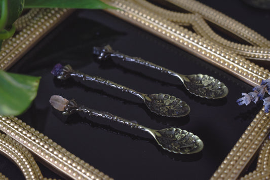 Vintage apothecary altar spoon with crystal, displayed on an obsidian mirror surrounded by herbs witchcraft ritual tool